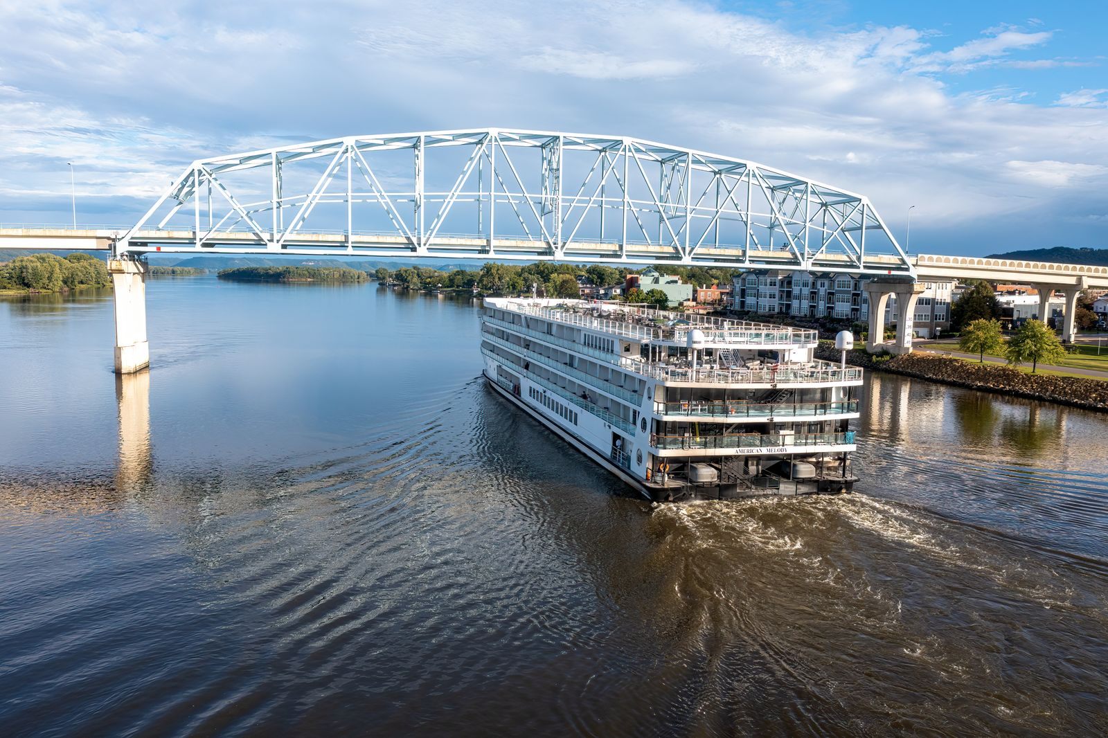 A modern multi-deck riverboat cruising under a steel truss bridge on the Upper Mississippi at Wabasha, Minnesota, on one of the US river cruises